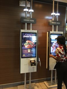 a woman is standing in front of two vending machines that are displaying fast food and order here