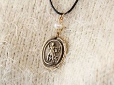 "Artemis Necklace, Goddess of Hunt and Moon, Wax Seal Pendant, Bronze Greek Jewelry, Intaglio Necklace, Diana Pendant, Huntress Necklace This unique and detailed handmade product is a beautiful bronze charm necklace inspired by an ancient releif statue of goddess Artemis holding a bow and arrows, wearing a short knee-high tunic and accompanied by a doe and a hunting dog.   Product Details - Approximate size: 2.5 cm X 2.2 cm (1\" X 0.87\"), without the bail ring and the pearl charm. - Material: Solid Bronze. - Fresh water pearl  - Adjustable cotton or leather cord. - Nickel and lead free. - Handmade intaglio pendant. *The pendant has been through an oxidization process with a liver of sulfur for an antique and vintage look.   *All products are handmade with our original intaglio seal design Artemis Necklace, Goddess Diana, Goddess Artemis, Wax Seal Pendant, Daughter Of Zeus, Classical Period, Necklace Moon, Hunting Dog, Greek Jewelry