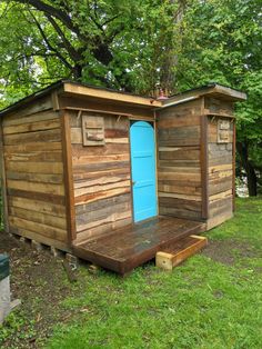 a small wooden outhouse sitting on top of a lush green field next to trees