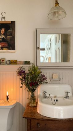 a white sink sitting under a mirror next to a wooden table with flowers on it