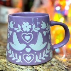 a purple coffee mug with white birds and hearts on it sitting on a counter top