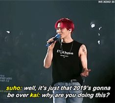 a man with red hair holding a microphone in front of a black background that says suho well, it's just that 2019's going to be over kil why are you doing this?