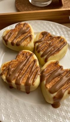 four heart shaped pastries with chocolate drizzled on them sitting on a white plate