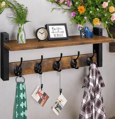 a wooden shelf with two hooks and some pictures hanging on the wall next to potted plants