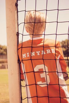 a young boy wearing an orange and white jersey standing in front of a soccer goal