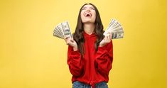 a woman in red shirt holding money up to her face with both hands and mouth open