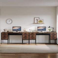 two computer screens sitting on top of a wooden desk next to a clock and window