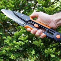 a person holding an orange and black knife in their hand next to some green leaves