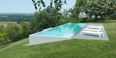 an empty swimming pool in the middle of a lush green field next to a white bench