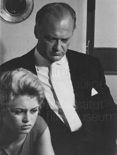 an old black and white photo of a man and woman looking at something on the table