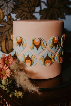 a pink cake sitting on top of a wooden table next to a flower vase and some feathers