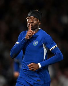 a male soccer player in a blue uniform is holding his finger up to his mouth