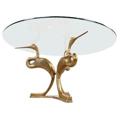 a glass table with two gold birds on it's legs and an oval glass top