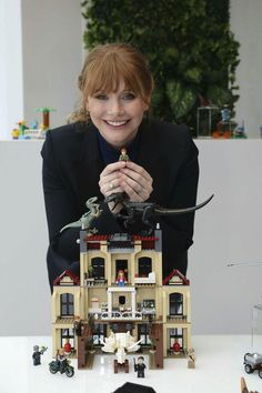 a woman sitting at a table in front of a toy house with dinosaurs on it