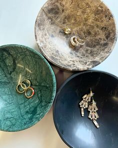 three different colored bowls with gold and silver rings in them on a white table top