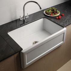 a white sink sitting on top of a counter next to a plate of vegetables and a knife