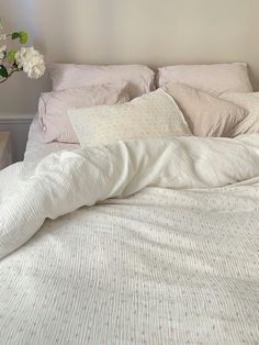 an unmade bed with white linens and flowers in a vase on the nightstand