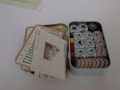 an open tin can filled with lots of different colored stamps and cards on top of a table