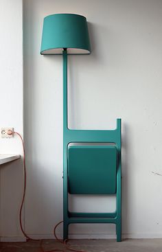 a green chair next to a white wall with a lamp on it