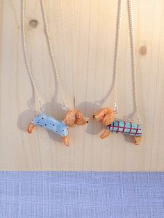 two small dogs wearing sweaters are hanging from necklaces on a wooden table top