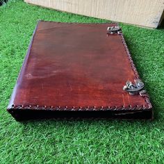 a brown leather notebook sitting on top of green grass next to a wooden box with two handles