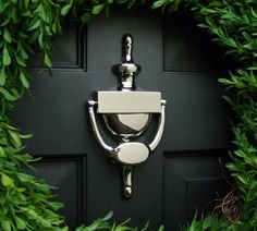 a toilet paper dispenser mounted to a black door surrounded by greenery