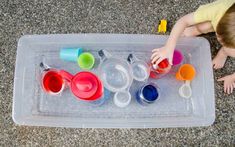 a young boy playing with plastic cups and spoons in an ice tray on the floor