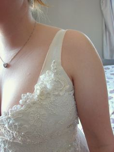 the woman is wearing a white dress and has a silver necklace on her neck while standing in front of a bed