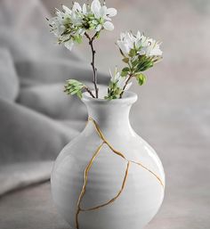 a white vase filled with flowers on top of a table next to a gray wall