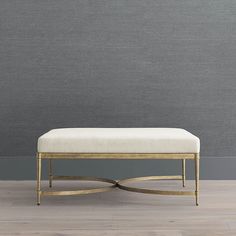 a gold bench with a white upholstered cushion on the floor in front of a gray wall