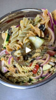 a spoon full of pasta and vegetables being held up by someone's hand over a metal bowl