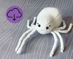 a white stuffed spider sitting on top of a bed next to a purple circle with an arrow