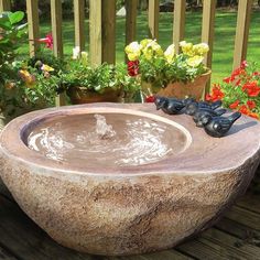 a stone bowl with water running from it on a wooden deck in front of flowers