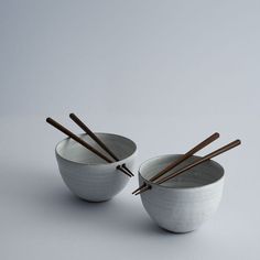 two white bowls with chopsticks in them