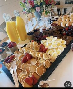 a table topped with waffles and fruit next to cups filled with orange juice