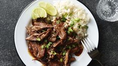 a white plate topped with meat and rice next to a glass of water on top of a table