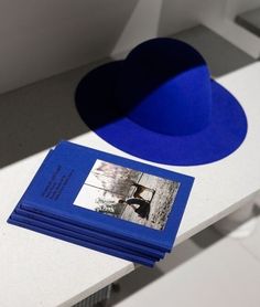 a stack of blue books sitting on top of a white table next to a black hat