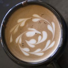 there is a cup of coffee with white designs on the foam in it's top