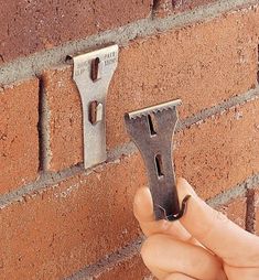 a hand holding a wrench in front of a brick wall that has two hooks on it