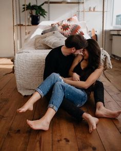 a man and woman sitting on the floor in front of a swing bed with pillows