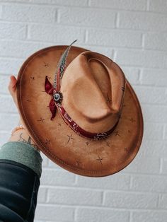 This wide brim fedora is a tan suede hat with hand burned crosses around the hat and an edge burn.  It is with a bandana, feathers, and rhinestone brooch. Cowgirl Concert, Edgy Cowgirl, Suede Hat, Hand Burn, Wide Brim Fedora, Rhinestone Brooches, Tan Suede, Fedora Hat, Wide Brimmed