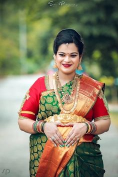 a woman in a green and red sari with gold jewelry on her neck, smiling at the camera