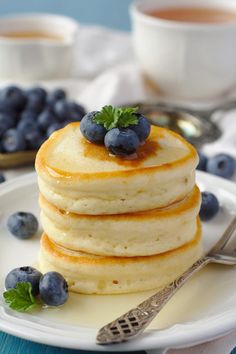 a stack of pancakes with blueberries and syrup on a white plate next to silverware