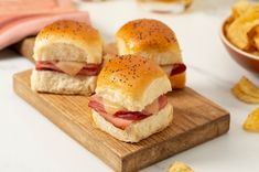 two ham and cheese sliders on a cutting board with potato chips next to it