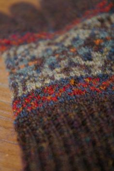 a close up view of a multicolored sweater on a wooden table with a cell phone in the foreground