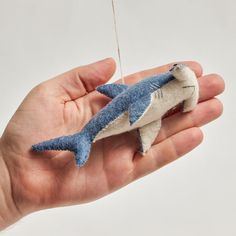 a hand holding a blue and white stuffed shark ornament in it's palm