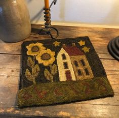 a rug with a house and sunflowers on it sitting on a wooden table