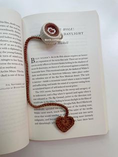 an open book with a string attached to it and a heart brooch on top