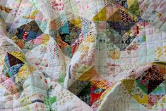 an old quilt is laying on top of a tablecloth covered with multicolored fabric