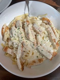 a white plate topped with chicken and pasta covered in gravy on top of a wooden table